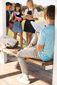 青少年男孩阅读书而同学则站在户图片