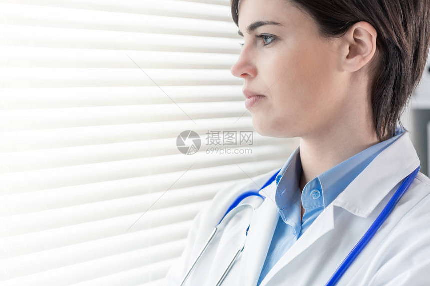 有吸引力的体贴的年轻女医生或护士站在高调的窗户外面图片