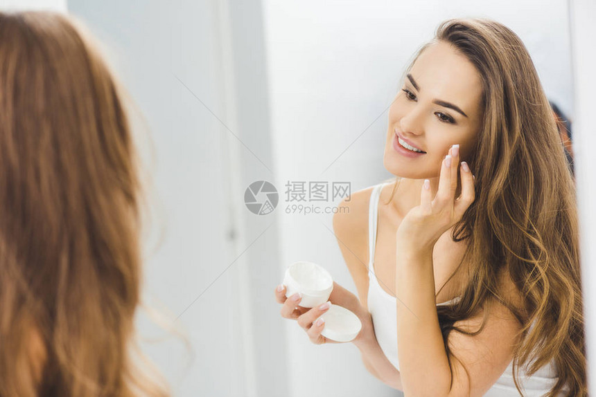 美丽微笑的女人涂面霜的镜面反射图片