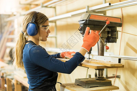 青年女木匠利用钻头在木车间工作的图片