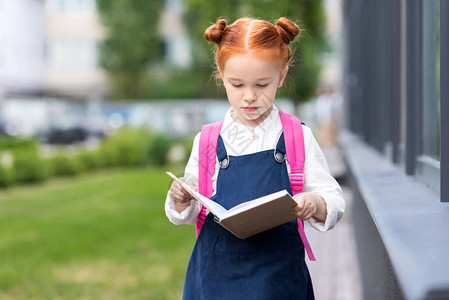 可爱的红发女学生背着书包在外面看书图片