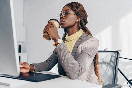 使用图形平板和在工作场所喝咖啡的美籍非洲女商人图片