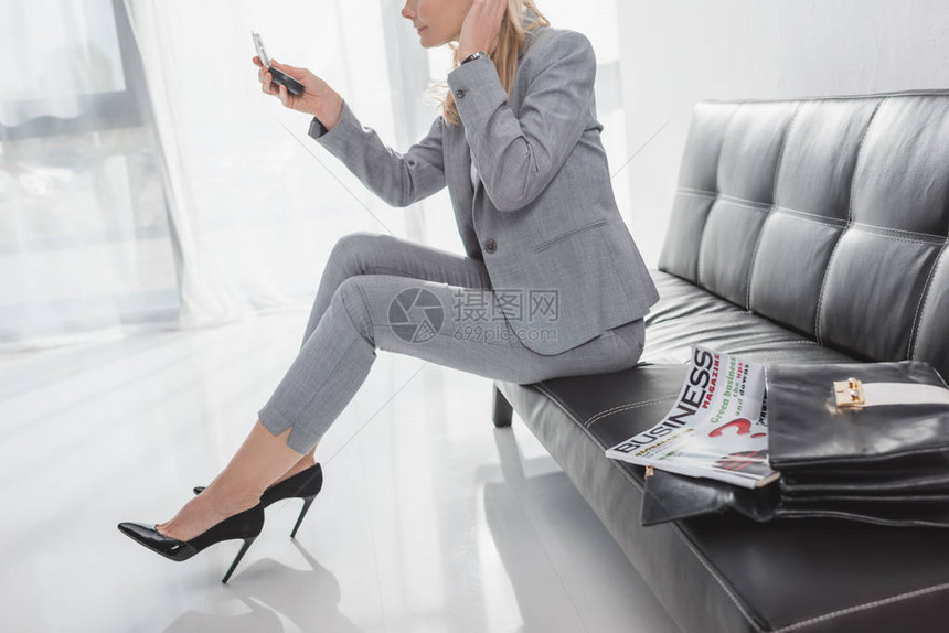 商业妇女坐在候诊室沙发上看化妆镜时图片