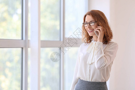 成功的商业女商人在办公室靠近窗口时通过手机说话在办公室的图片