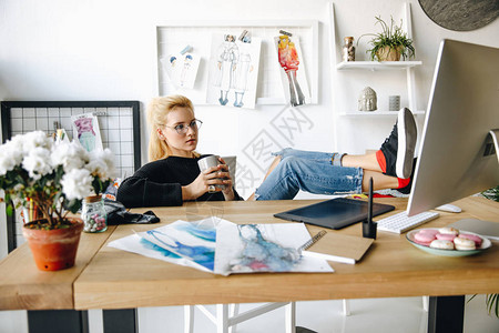 有吸引力的年轻时装设计师在眼镜喝咖啡和在办公室图片