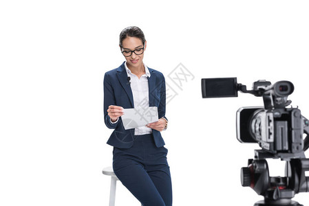 美丽的微笑着的女新闻播报员报纸坐在镜头前在背景图片