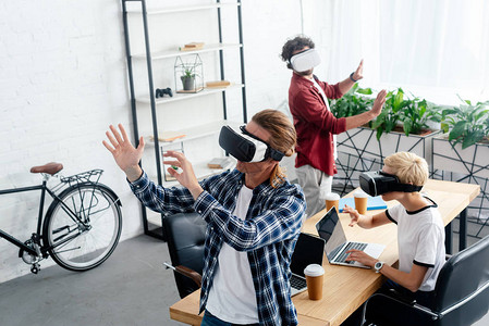 工作单位使用虚拟现实头戴的年轻启动团队高角度图片