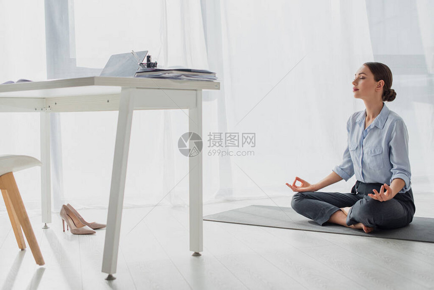 年轻女商人在莲花的位置上做瑜伽在办公室的垫子上和吉安泥图片