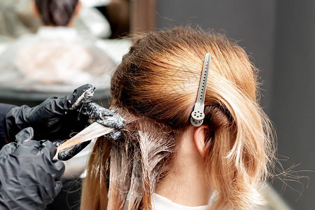 美发师用黑手套戴着女人染发的头图片