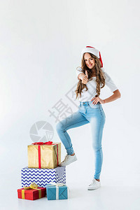 穿着圣诞礼帽的快乐女孩站在圣诞节礼物盒旁边举起拇指图片