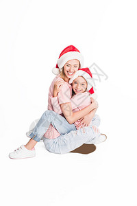 母亲和女儿笑着戴圣塔帽子拥抱在地上图片