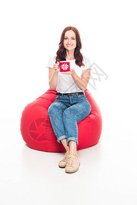 快乐的女孩喝着一杯咖啡坐在红豆袋椅上孤图片