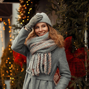 穿着时尚灰色外套戴着针织帽和时尚围巾的快乐风趣的年轻女子在街上靠近一家咖啡馆背景图片
