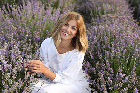 穿着白裙子的有笑容的女子坐在紫衣花草田图片