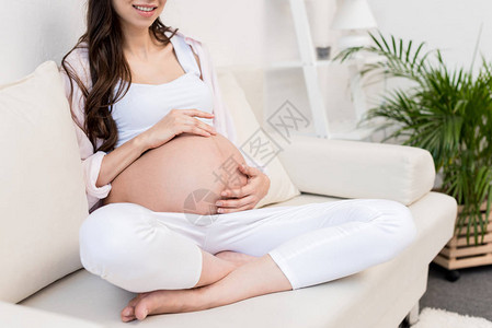 孕妇坐在的沙发上摸着肚子图片
