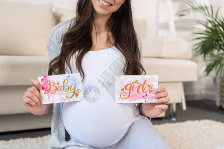 坐在客厅里坐在地板上的孕妇持有两张带女婴图片