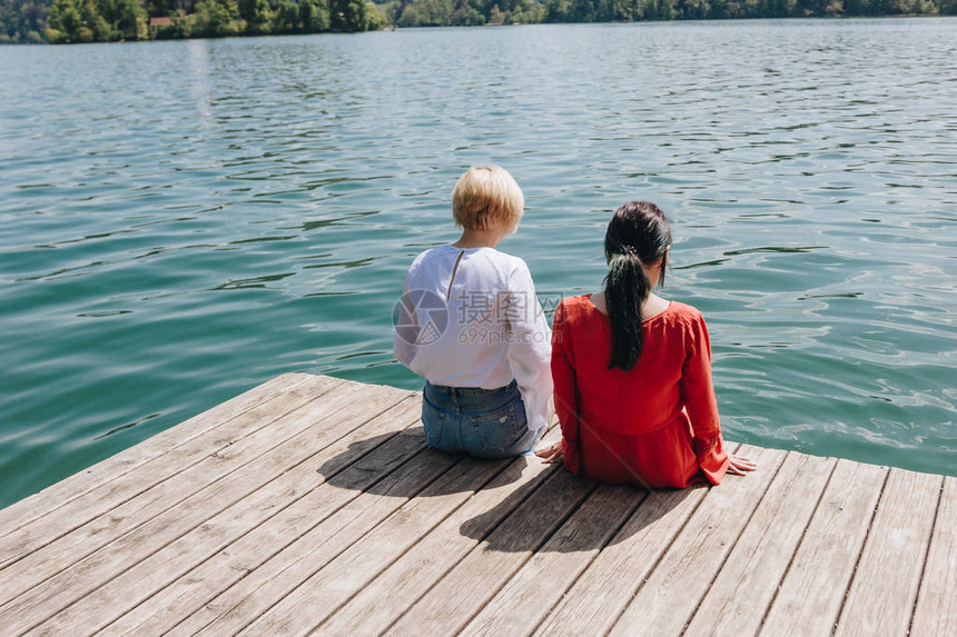 两名年轻时尚女坐在湖边的木码头上流着鲜图片