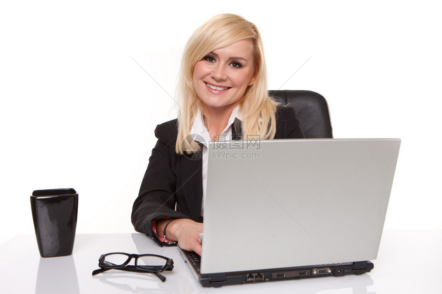 戴眼镜的漂亮金发女商人在她桌子上的笔记本电脑上工作图片