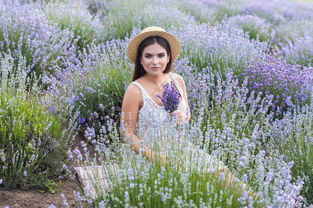 穿着白裙子的漂亮女人坐在紫衣花草田里图片