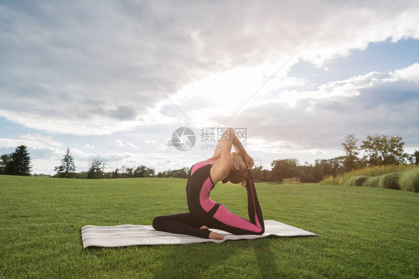 女在公园绿草坪上做一只脚鸽子瑜伽图片