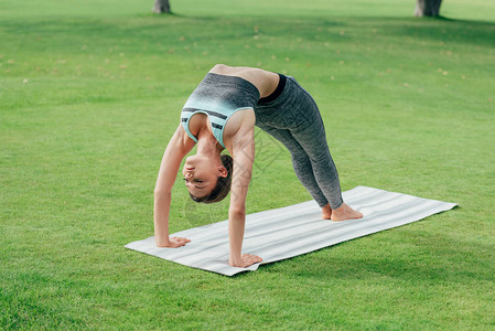 参加运动服的女在公园练习瑜伽轮姿势图片
