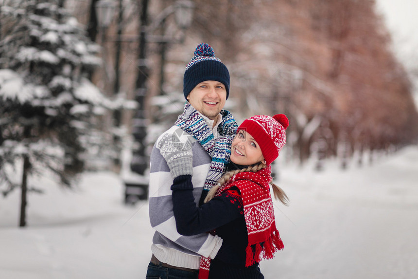 一对情侣可爱的毛衣用来在雪地冬季公园散步图片
