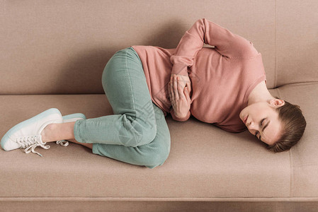 在沙发上躺着的不快乐的妇女肚子痛图片