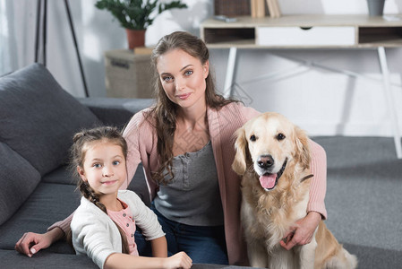 年青母亲和女儿与他们的狗坐在起居室的地板上图片