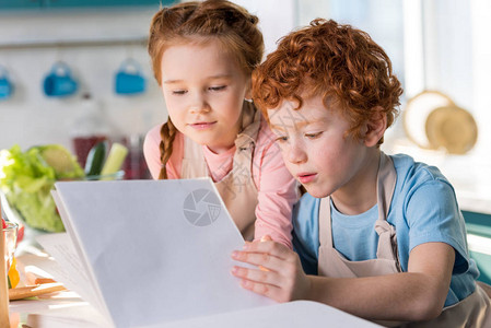 儿童在厨房一起做饭的同时看烹饪书在图片