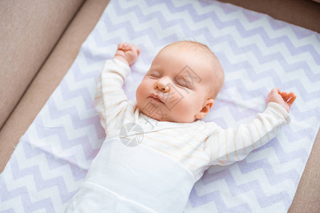 可爱的婴儿闭着眼睛举起双手躺在沙发上图片