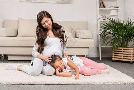 孕妇坐在毛毯上她的女儿躺在大腿上图片