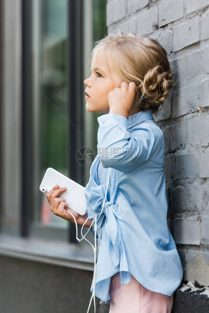耳机中可爱孩子的一面手持智能手机图片