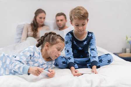 年轻的男孩和女孩坐在床上玩智能手机图片