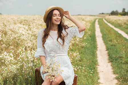 穿着白衣服的笑着女人野生卡莫米花束在田里坐在背景图片