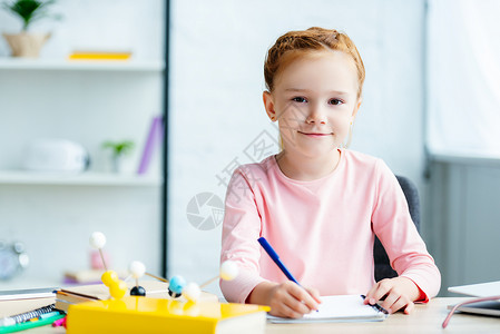 美丽的红发美女学生在书桌上写笔记本图片