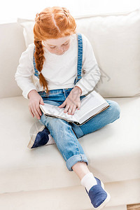 坐在沙发和阅读书上的可爱小女孩图片