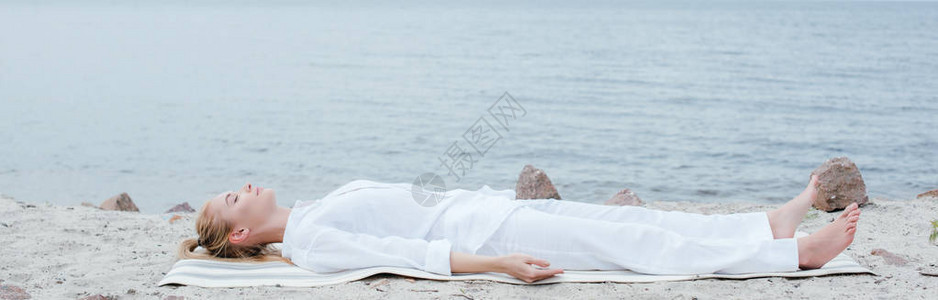 在海边的瑜伽垫上躺着时闭着眼睛冥想着光着图片