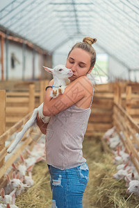 美丽的女人在农场拥抱和亲吻山羊图片