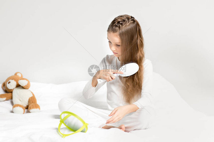 穿着睡衣坐在床上和梳发的可爱小女孩图片