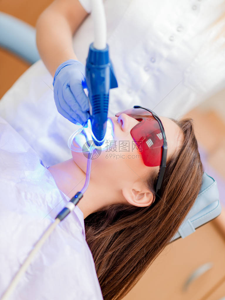 去看牙医办公室的美丽的年轻女士她用紫外线灯在牙齿图片
