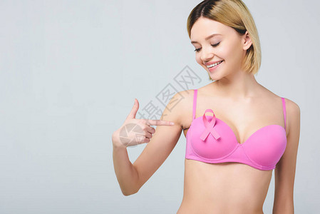 美丽的微笑着的美丽女人指着粉红胸罩带有乳癌意识丝带图片