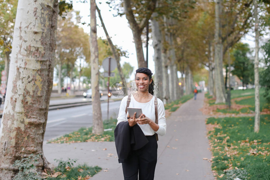 美丽的黑人女下课后带着平板电脑走在落叶的街道上国际交流和现图片
