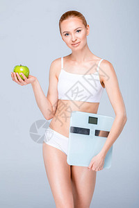 身穿白内裤持有数字比例尺和在灰色上孤立的绿苹果的白内衣图片