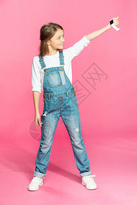 穿着牛仔服的可爱小女孩带着聪明的手表笑着在粉红图片