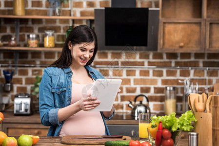 微笑着的年轻孕妇在厨房做饭时使用图片