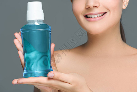 裸露肩膀的微笑女人拿着被灰色隔离的漱口水的部分看法图片