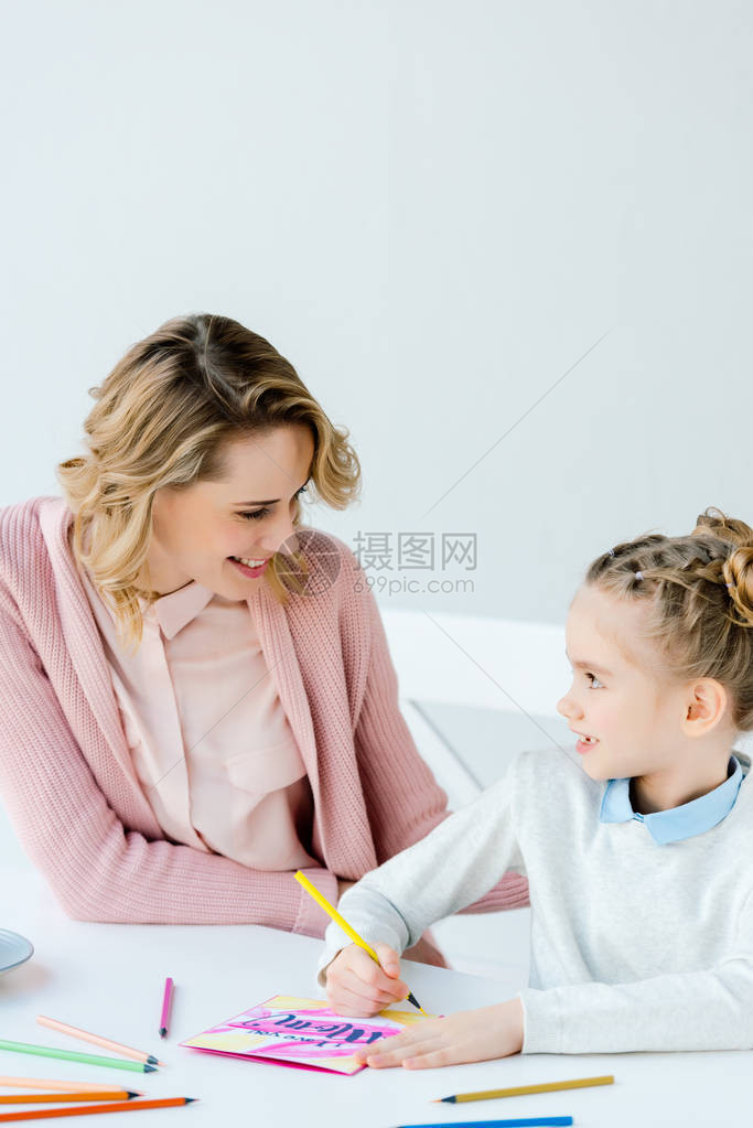 微笑的母亲看着女儿在餐桌上图片