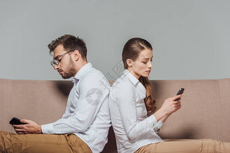 年轻夫妇背靠坐在一起使用在灰色上隔图片