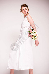 身着白裙子的年轻美女拿着鲜花望背景图片