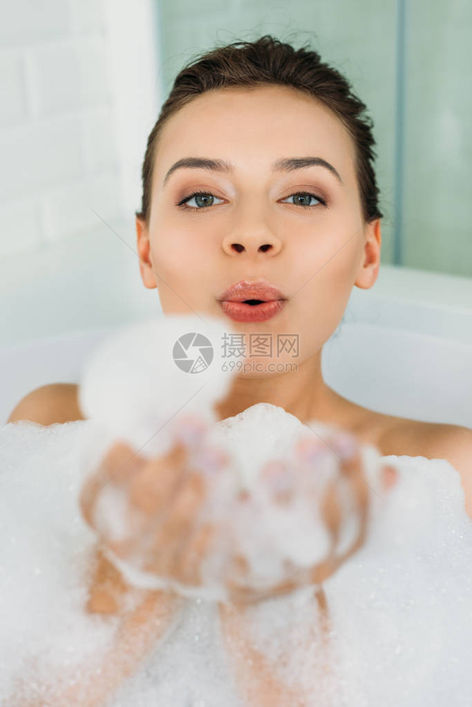 美丽的年轻女士在浴室里吹发泡图片